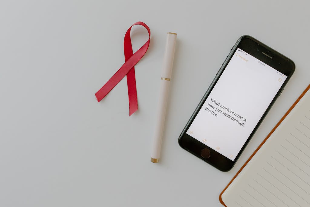 Pink Ribbon as a Symbol of Breast Cancer and a Smartphone Displaying a Text Lying on White Background