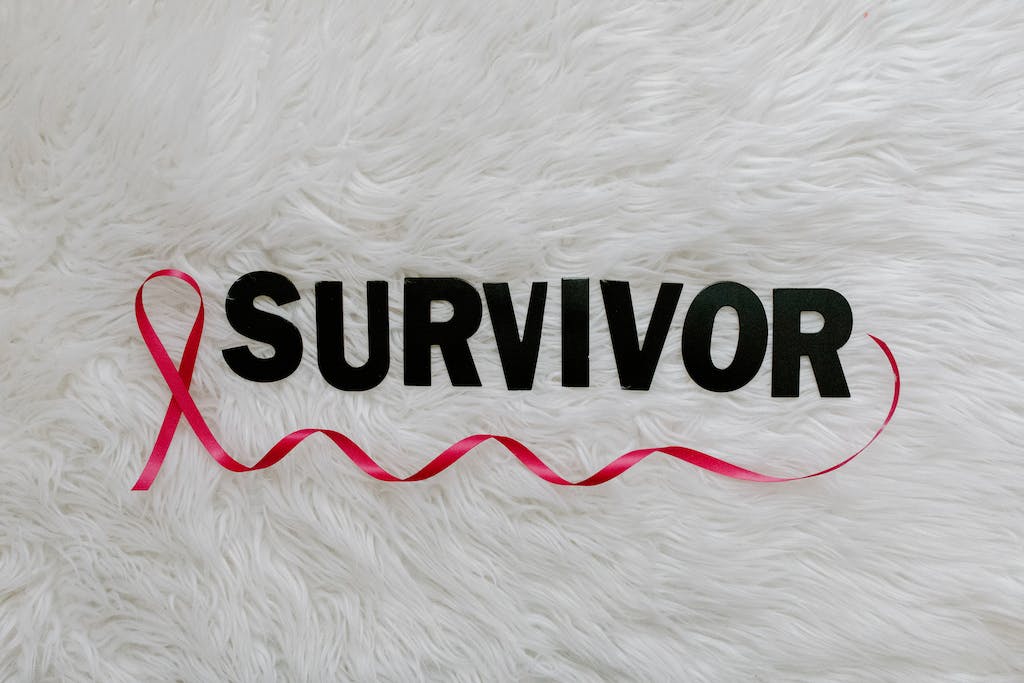 Text Saying "Survivor" an a Pink Ribbon Symbolizing Breast Cancer Lying on White Background