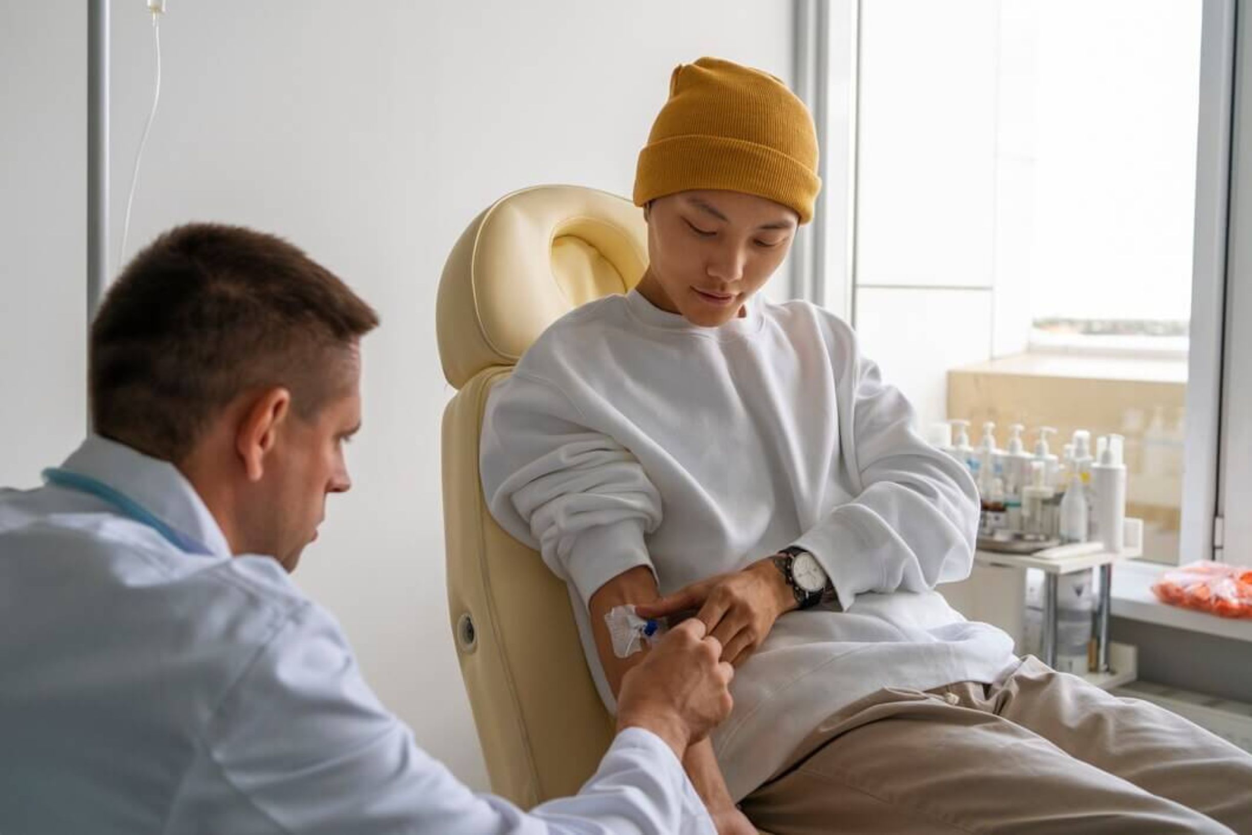 A healthcare professional assisting a cancer patient wearing a yellow beanie during a treatment session in a Cancer Concierge Service